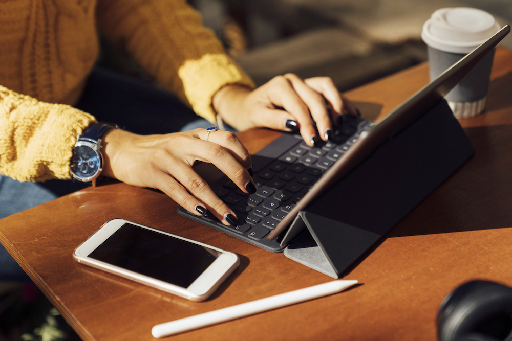 Close up of woman’s hands working with a tablet and smartphone at a café, mobile devices empowered for remote work by mobile device management MDM